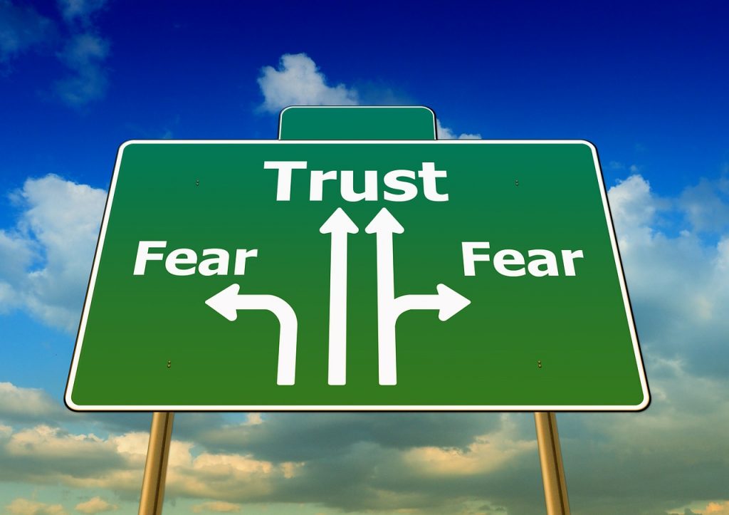 Green sign with white arrows and the words "trust" and "fear" on it.