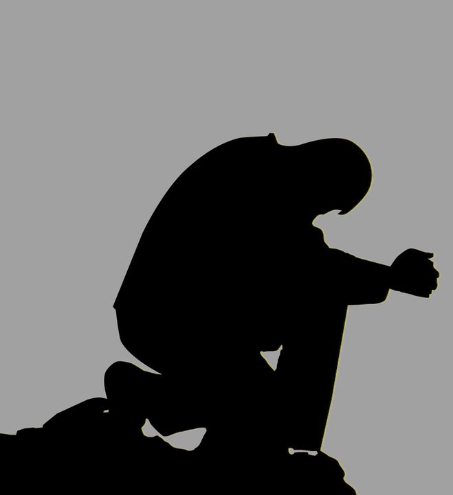Silhouette of person kneeling with hands clasped in front of him, with head down.